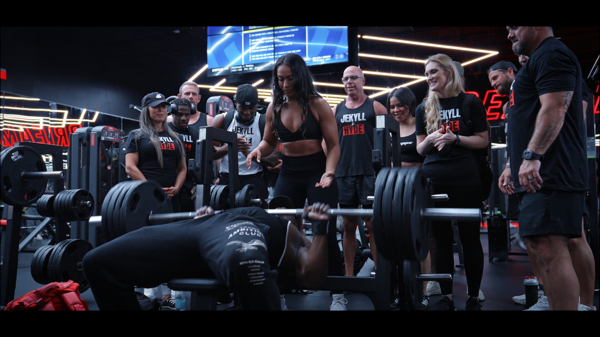 Shamaira coaching a lifter through a heavy bench press while the group watches